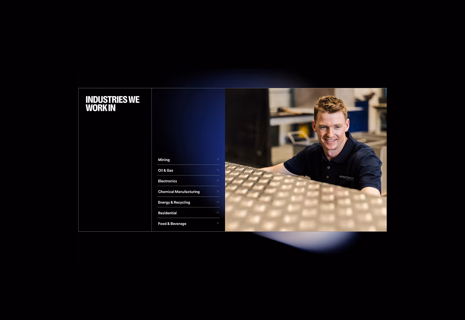 Smiling worker in a Spectrum-branded polo shirt inspecting a large metal plate in a workshop.