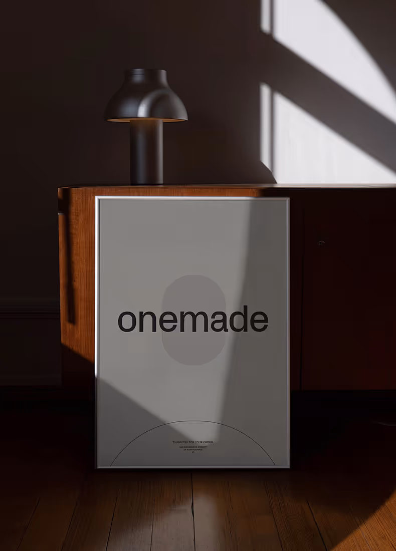 Framed Onemade poster resting on a wooden cabinet beside a modern lamp.