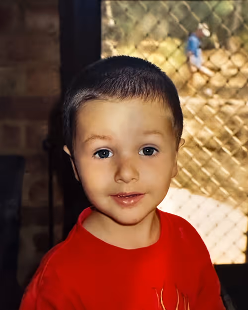 Childhood photo of a young boy with short hair wearing a red shirt, standing indoors with a soft smile—used as part of a playful team profile for Four Stripes.