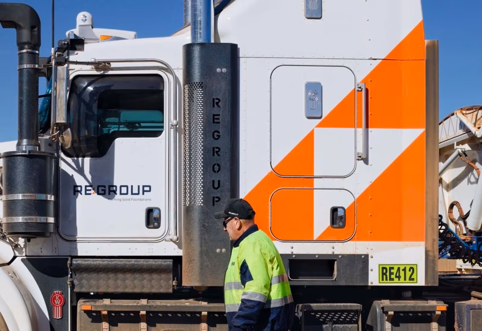 White and orange REGROUP truck with logo and worker in high-vis uniform.