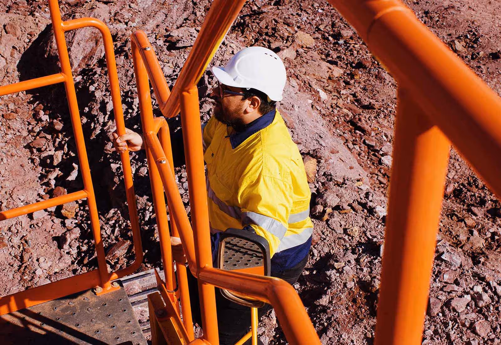 Worker in hard hat and high-vis jacket climbing orange metal stairs on site.