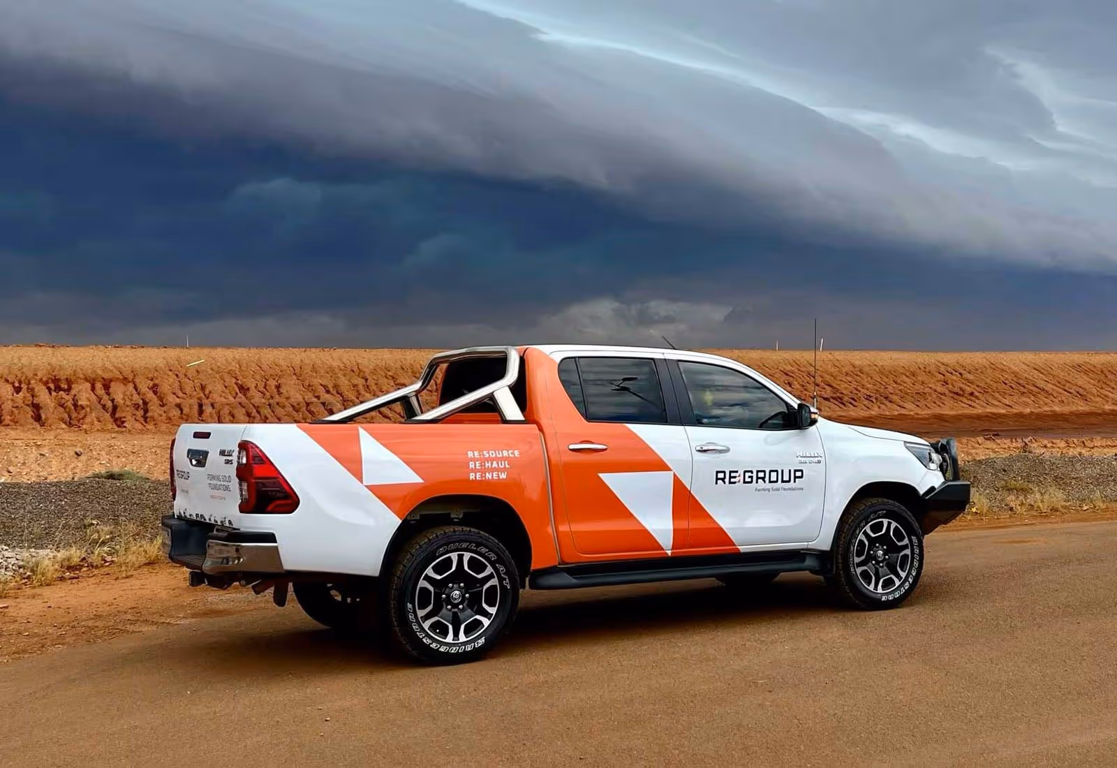 White and orange REGROUP utility vehicle parked on rural road under stormy sky.