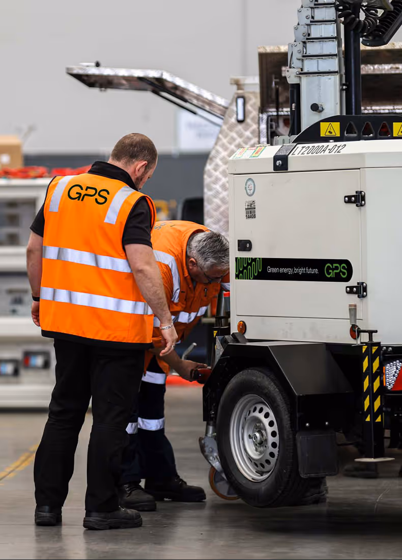 Two workers in orange safety vests servicing a GPS-branded generator inside a facility