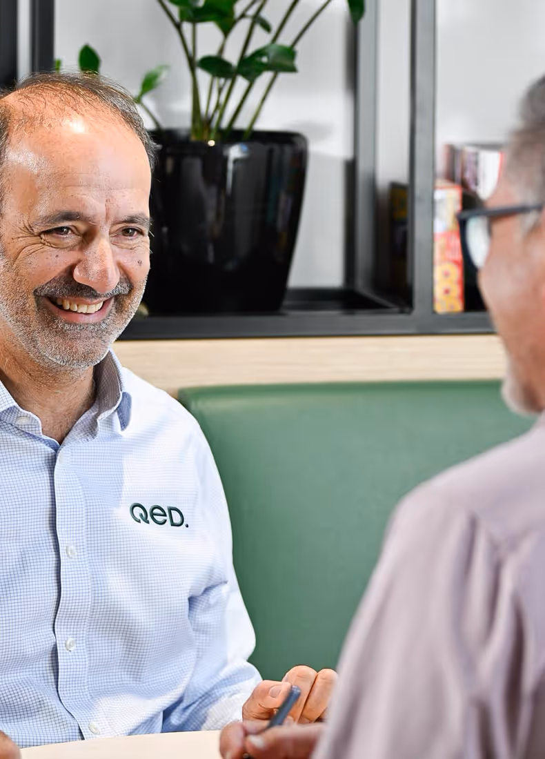 QED employee smiling during a meeting, wearing branded company shirt, conveying professionalism and approachability.
