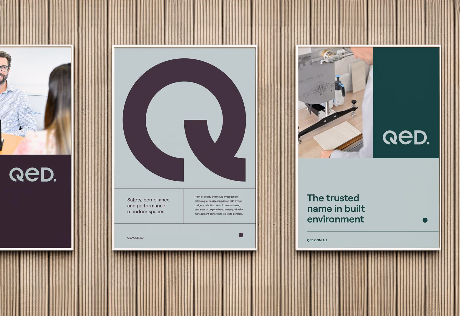 A set of three vertical QED posters mounted on a wooden wall, each showcasing core brand messaging around compliance, trust, and built environments.