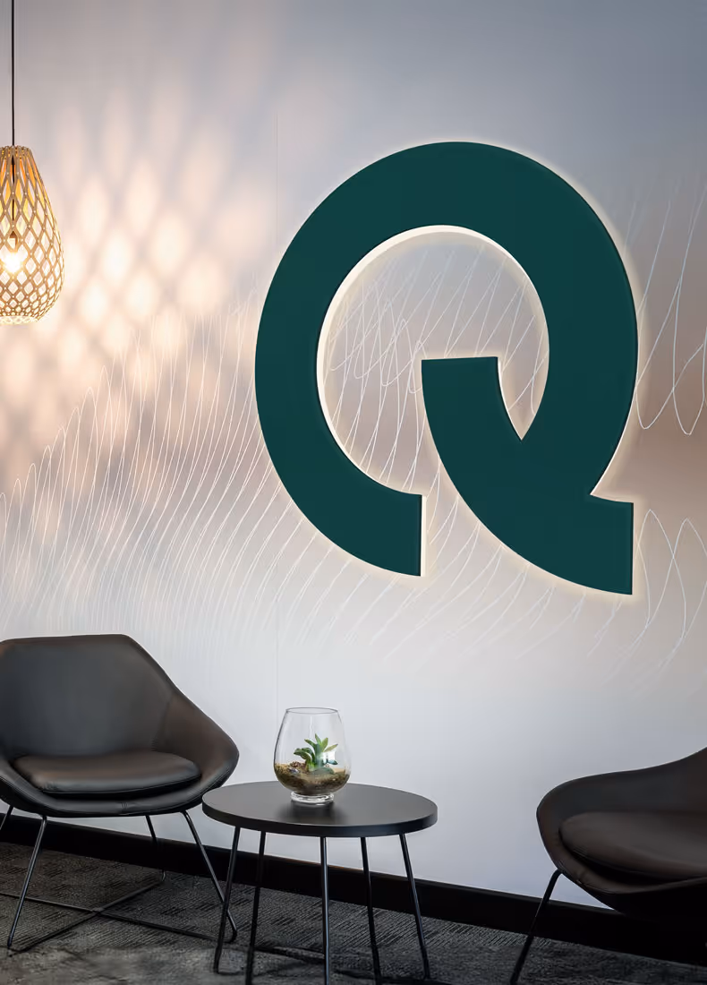 A large illuminated QED "Q" logo wall feature in an office seating area, enhancing the brand’s spatial identity and welcoming atmosphere.