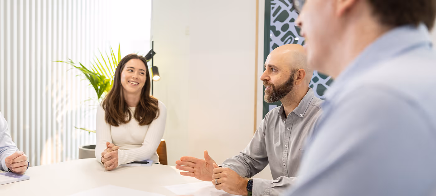 Team members engaged in a collaborative strategy session in a bright, plant-filled meeting space, exchanging ideas with focus and ease—representing Four Stripes’ expertise in strategic thinking and human-centred brand direction.