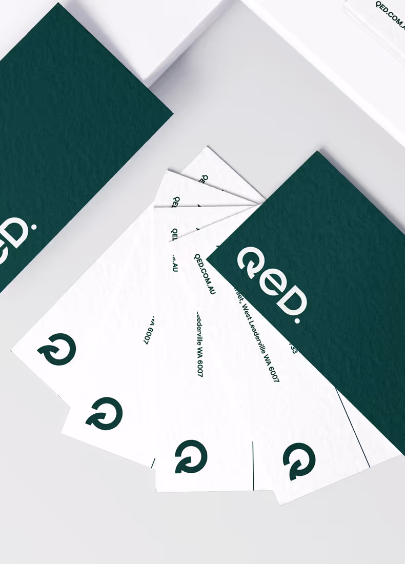 QED business cards laid out in a fanned arrangement, featuring a clean, minimal design with brand colors and address details.