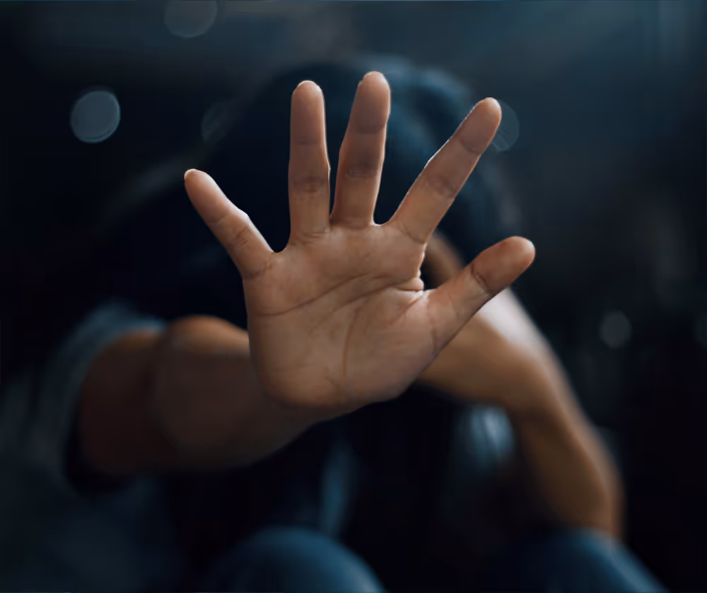 Ausgestreckte Hand mit der Handfläche nach vorne vor einer Person mit gesenktem Kopf, die eine Geste des Anhaltens oder der Abwehr vermittelt.