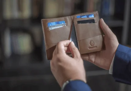 Person, die eine offene braune Lederbrieftasche mit sichtbaren Kreditkarten darin hält.