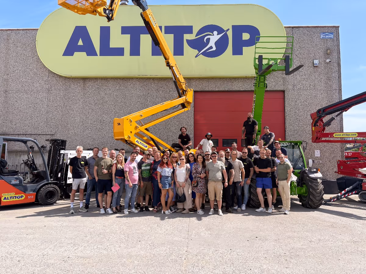 Groupe d'employés devant un bâtiment avec logo ALTITOP et matériel de levage jaune et vert.