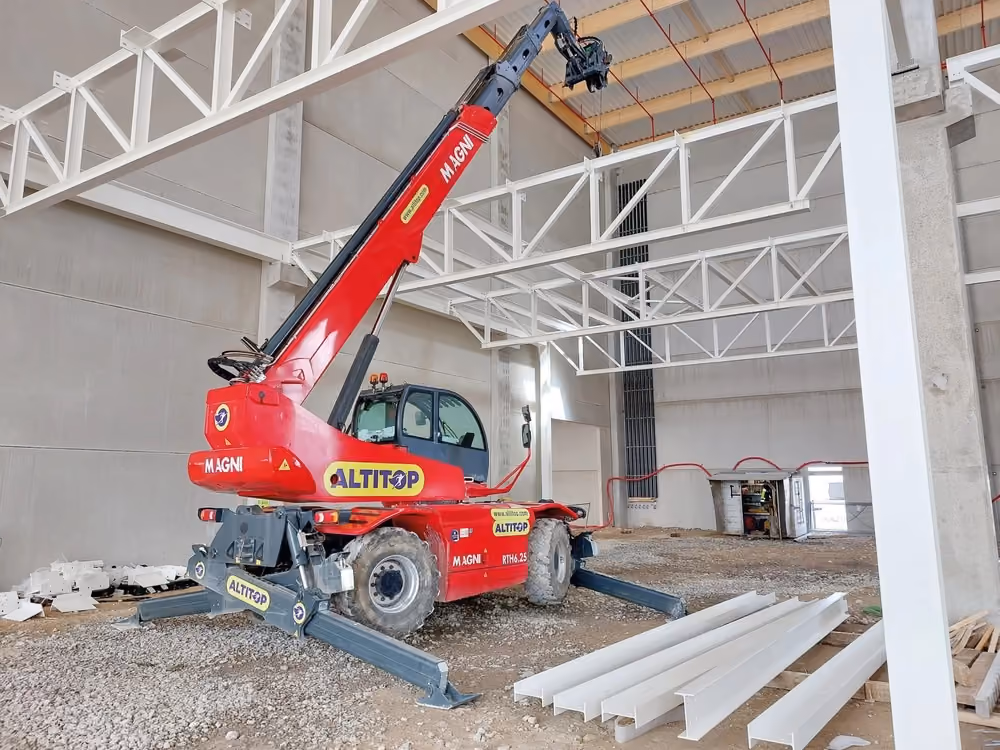 Chariot télescopique rouge Magni avec stabilisateurs dans un bâtiment en construction.