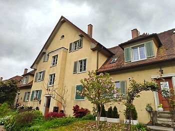 Gelbes Mehrfamilienhaus aus den 1920er Jahren mit grünen Fensterläden