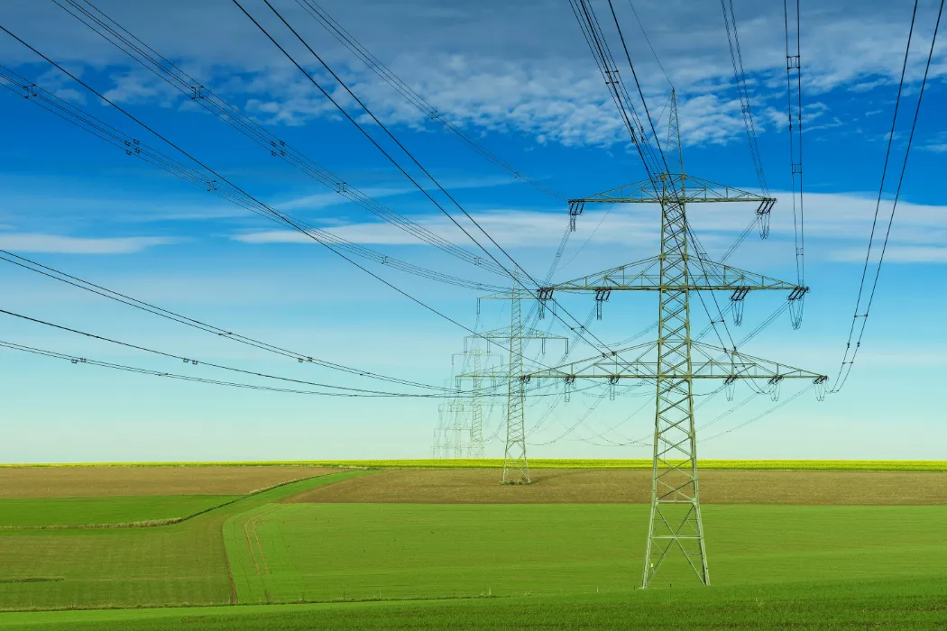 Hochspannungsleitungen über einem grünen Feld bei blauem Himmel