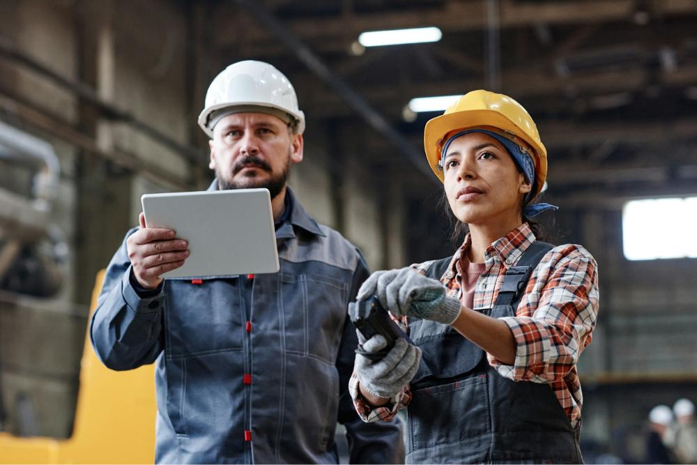 Zwei Ingenieure mit Schutzhelmen und Westen in einer Produktionshalle