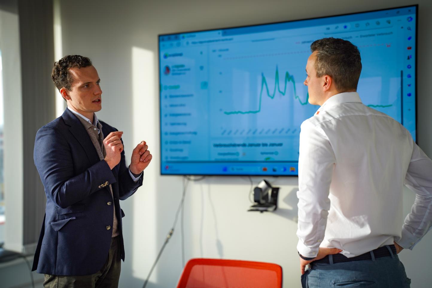 Zwei Männer im Anzug diskutieren vor großem Display