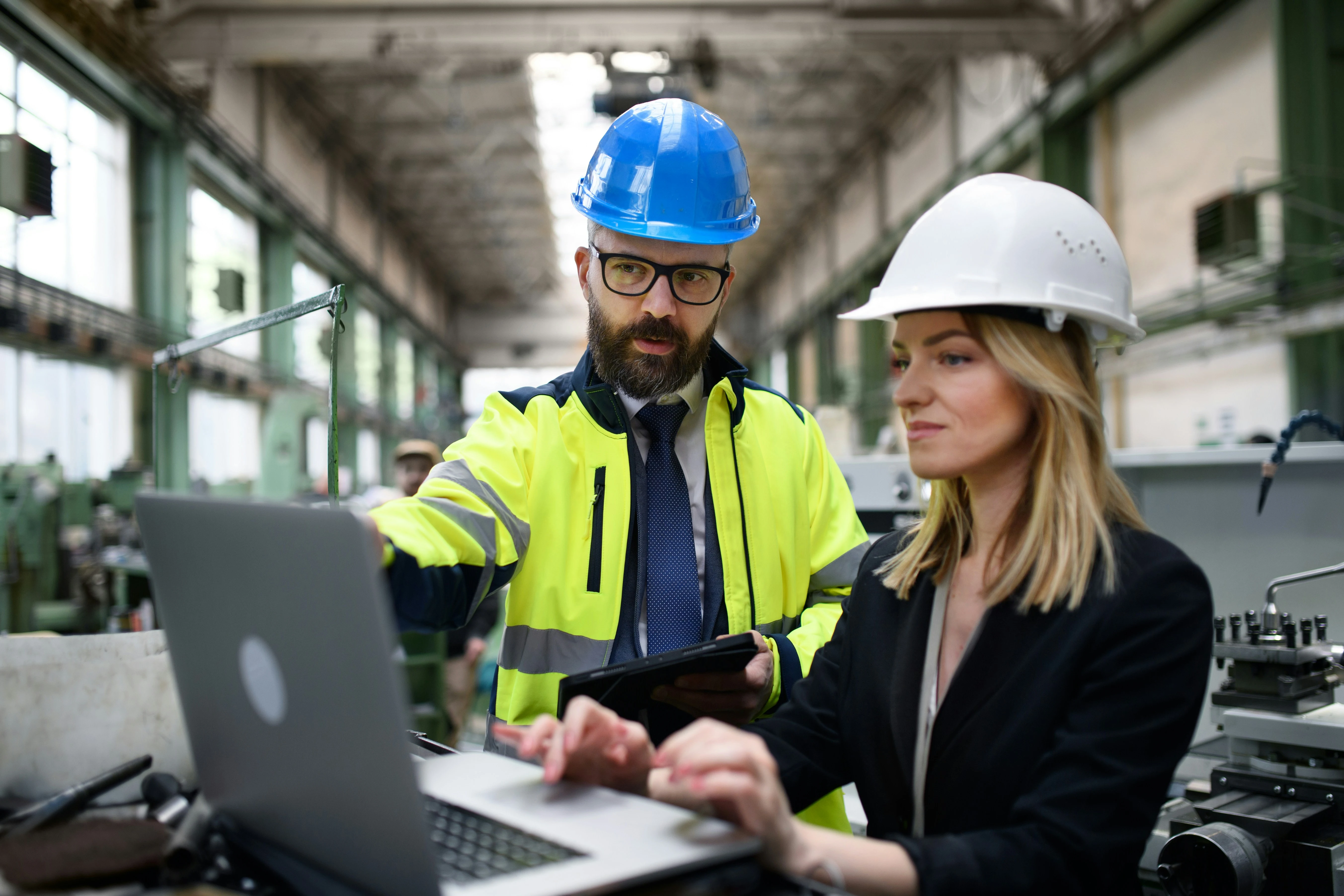 Ingenieur und Ingenieurin mit Helmen arbeiten am Laptop in Fabrikumgebung