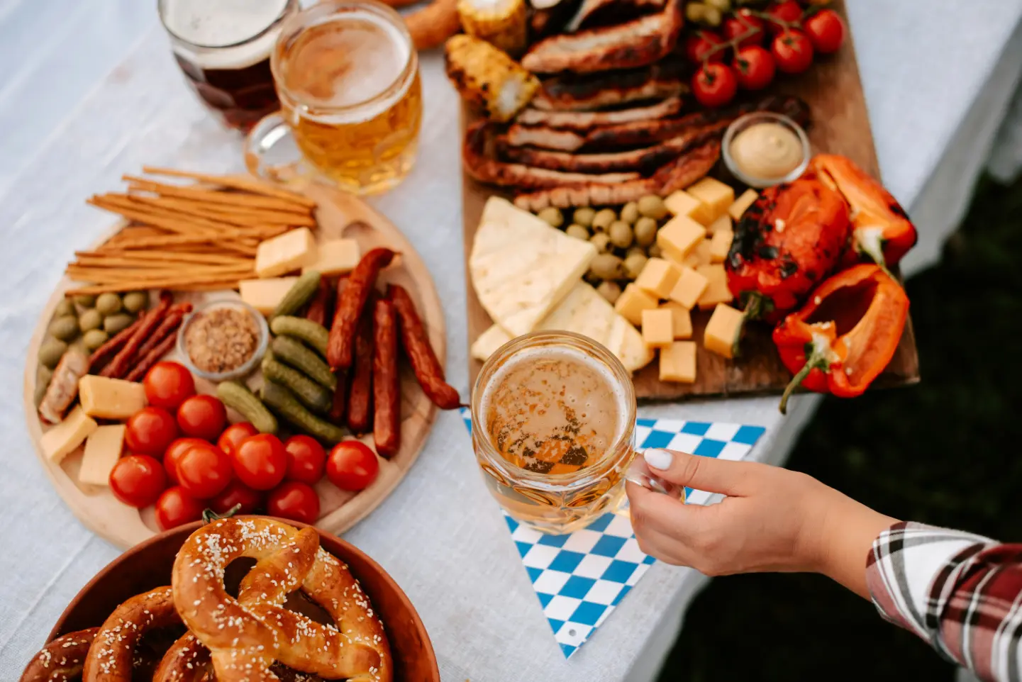 „Bayerische Brotzeit mit Bierkrügen, Brezeln, Käse, Wurst und gegrilltem Gemüse auf Oktoberfest-Tisch