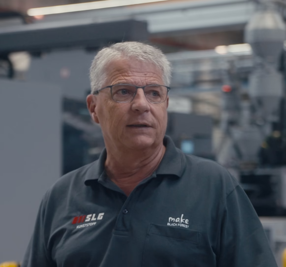 Älterer Mann mit grauen Haaren in Arbeitskleidung in einer Produktionshalle