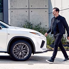 A customer walking around a Lexus to get in the vehicle.