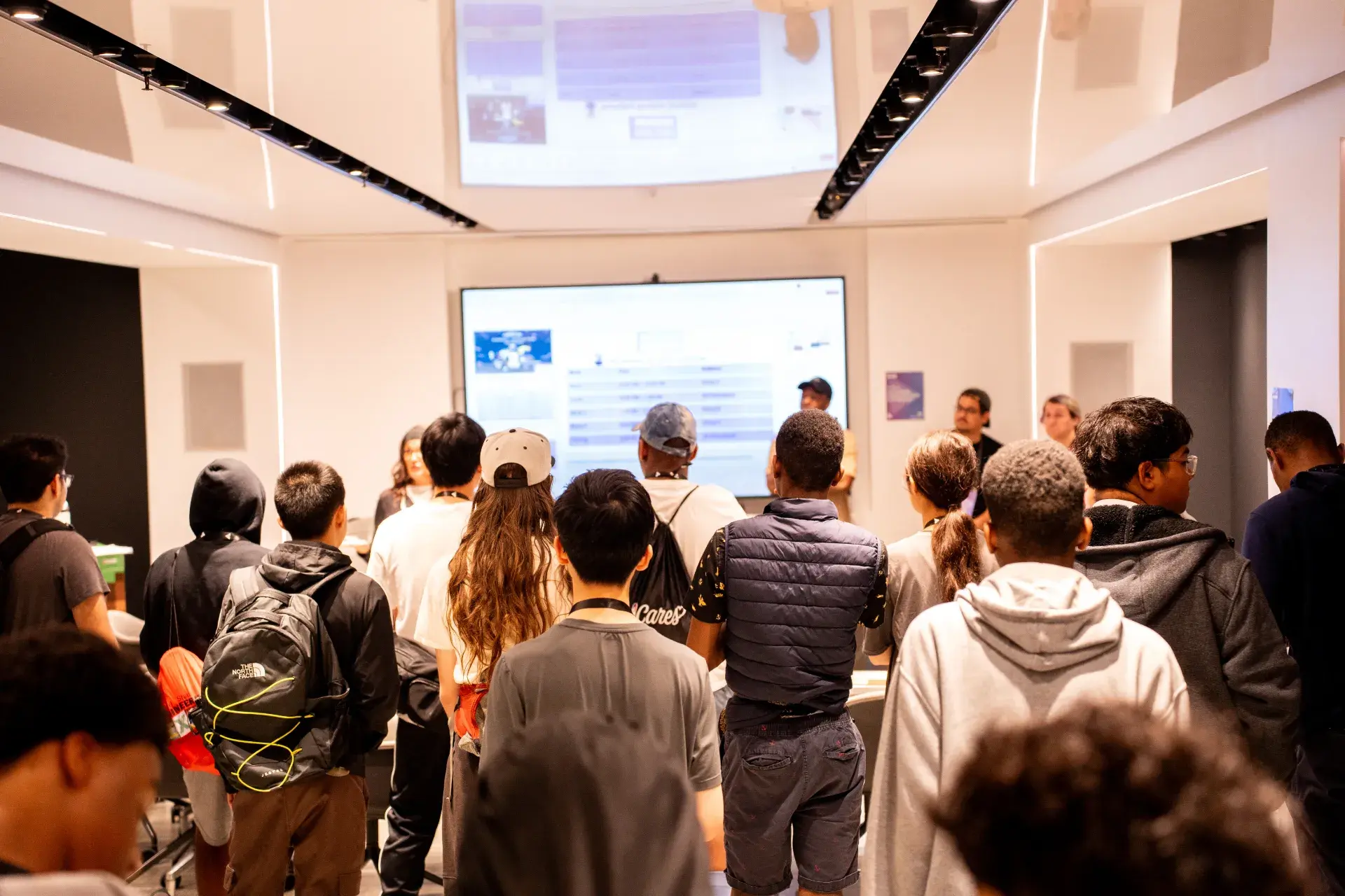 Audience watching presentation on large screen in modern white room