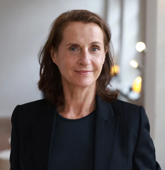 Frau in einem schwarzen Blazer vor einer Betonwand.