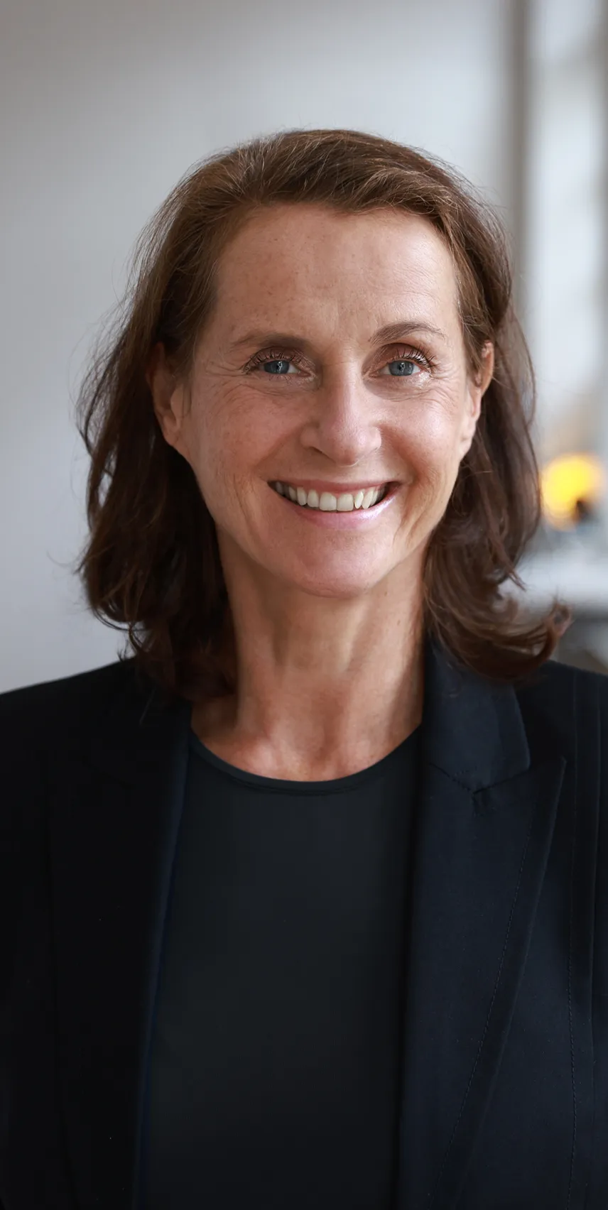 Frau in einem schwarzen Blazer vor einer Betonwand.