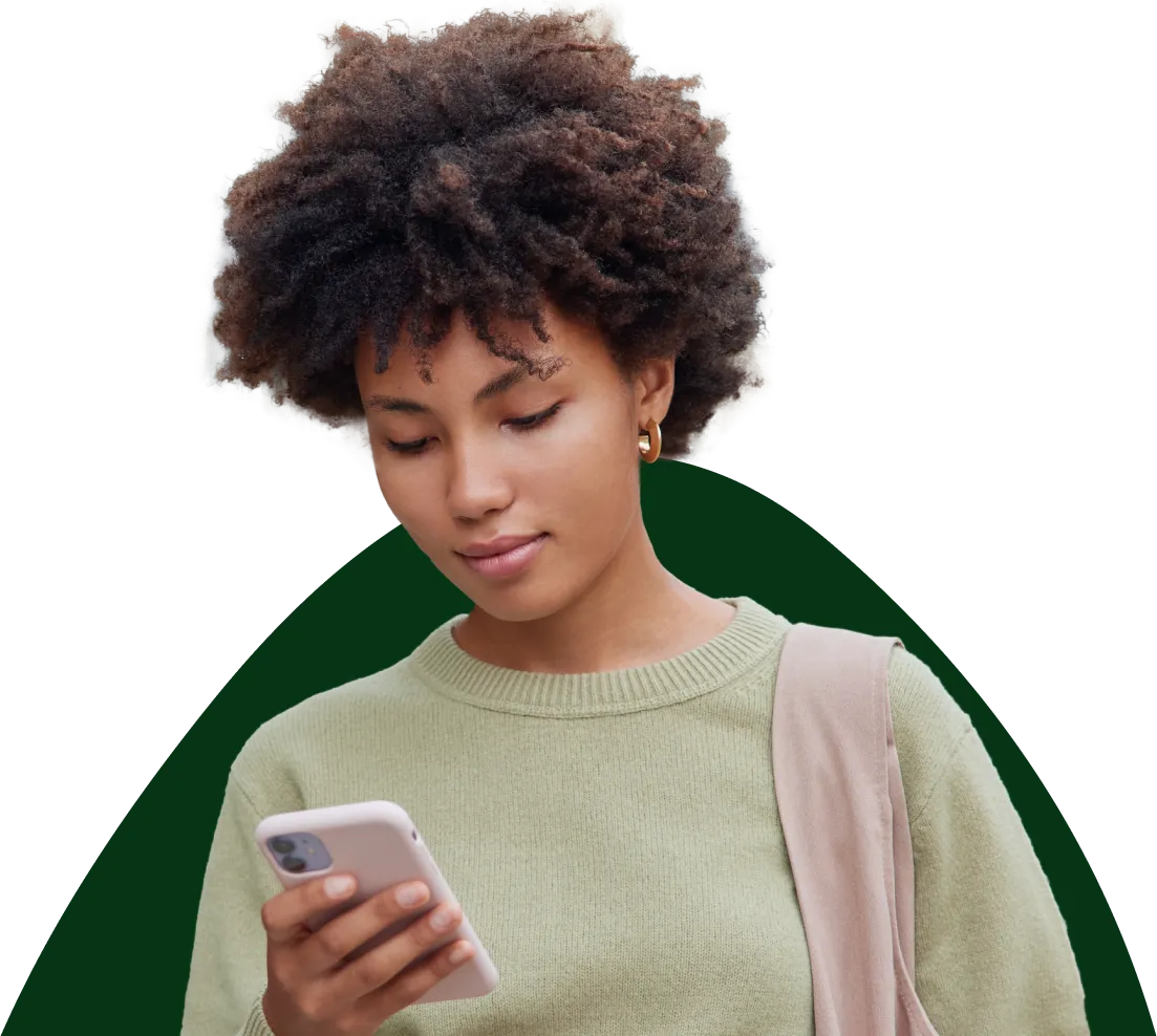 Young woman with curly hair wearing a light green sweater and a beige shoulder bag looking at her smartphone.