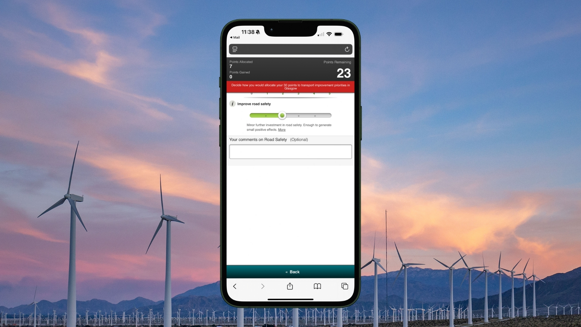 Mobile phone screen displaying a transport improvement app with a slider to allocate points for road safety, set against a backdrop of wind turbines at sunset.