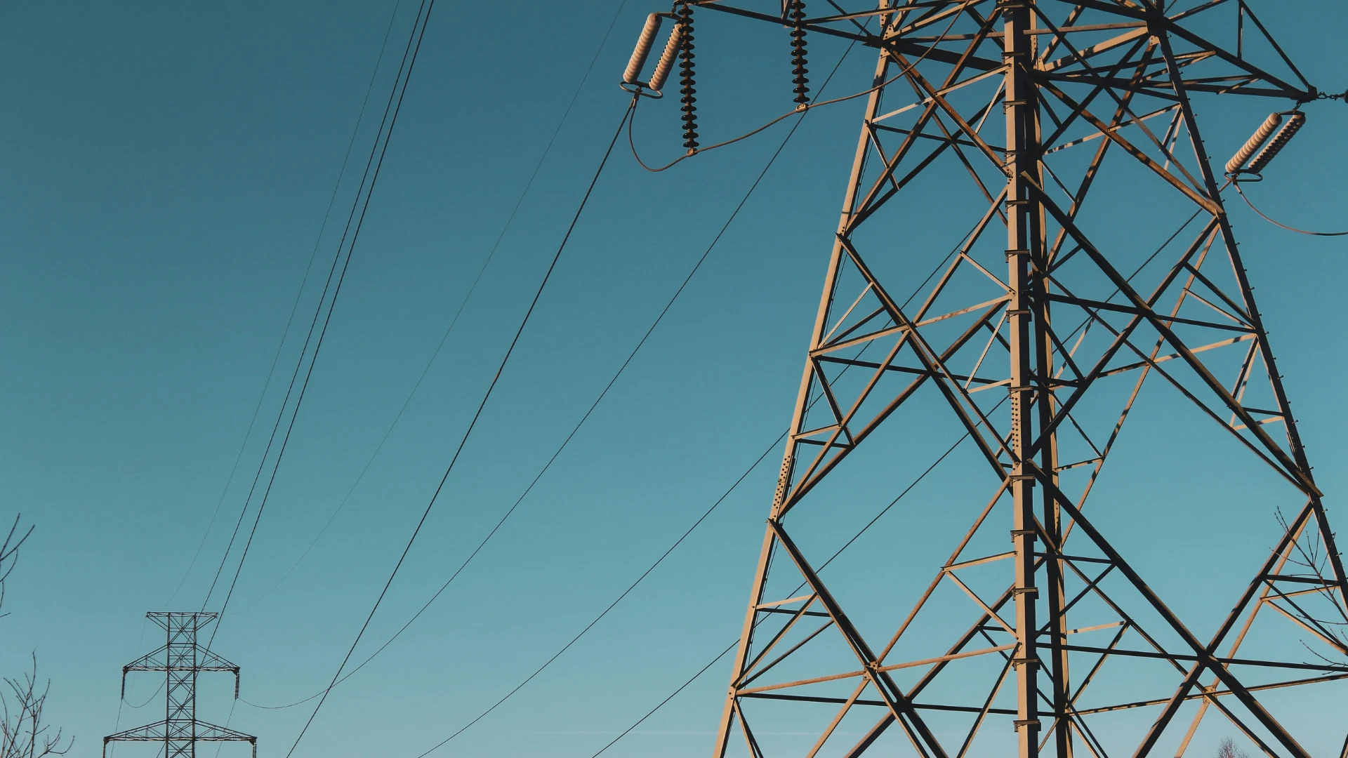 Large metal electrical transmission towers with power lines against a clear blue sky.