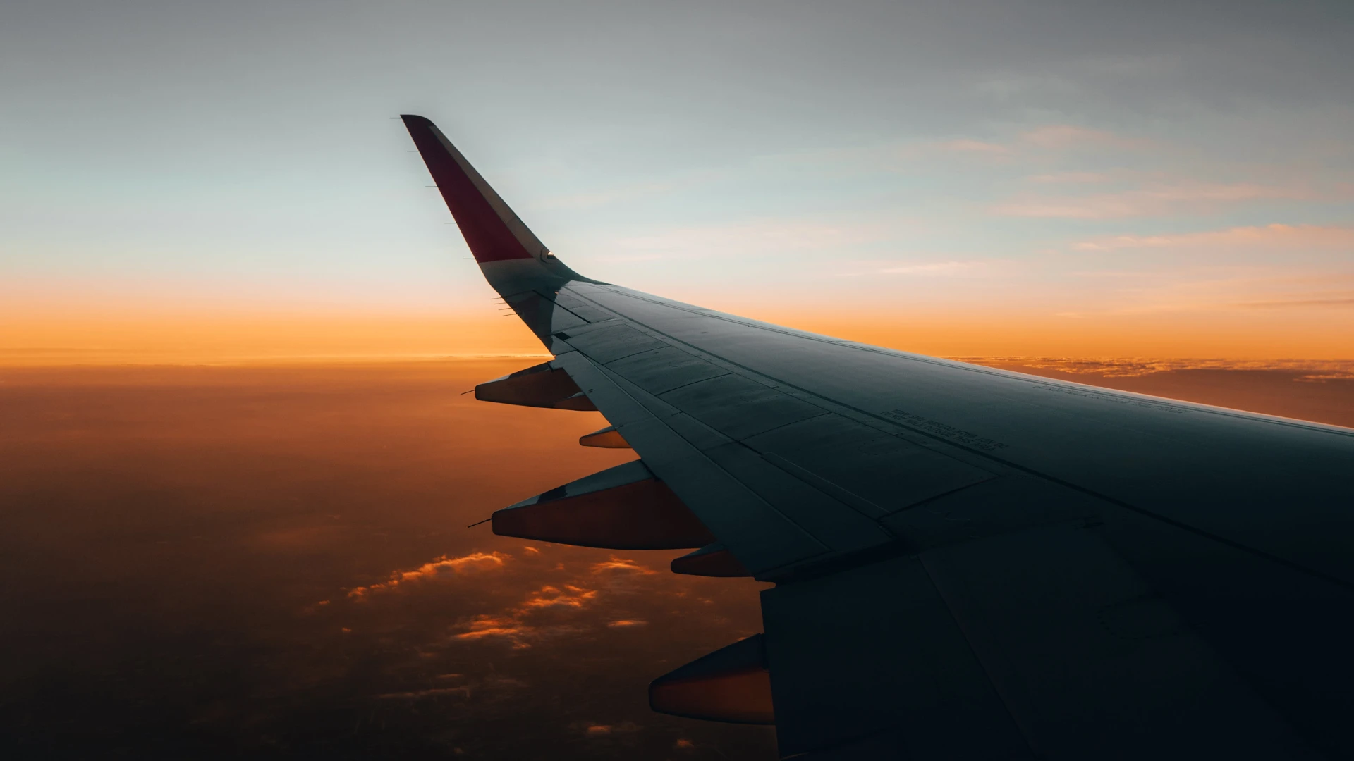 Airplane wing in flight against a sunset sky with orange and blue tones.