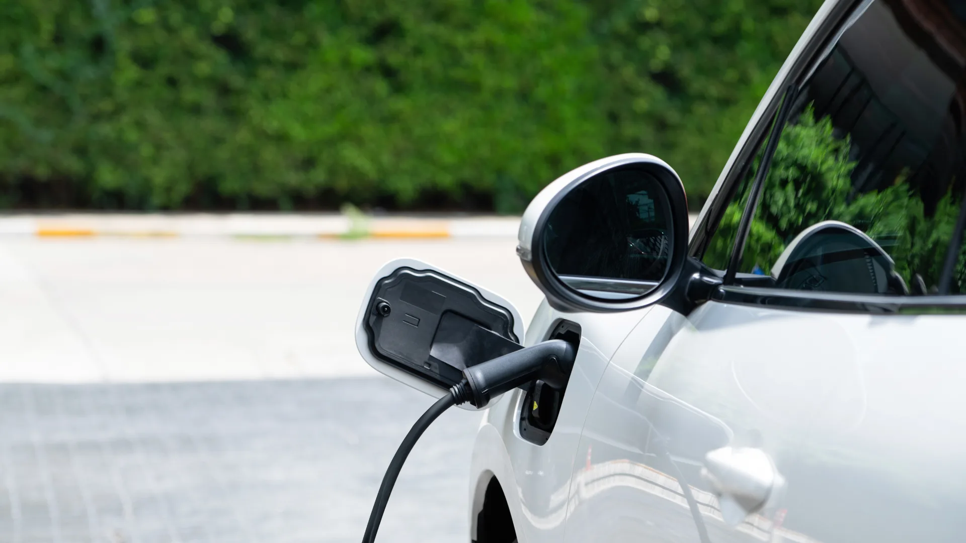 White electric car charging with a cable plugged into the charging port near the side mirror.