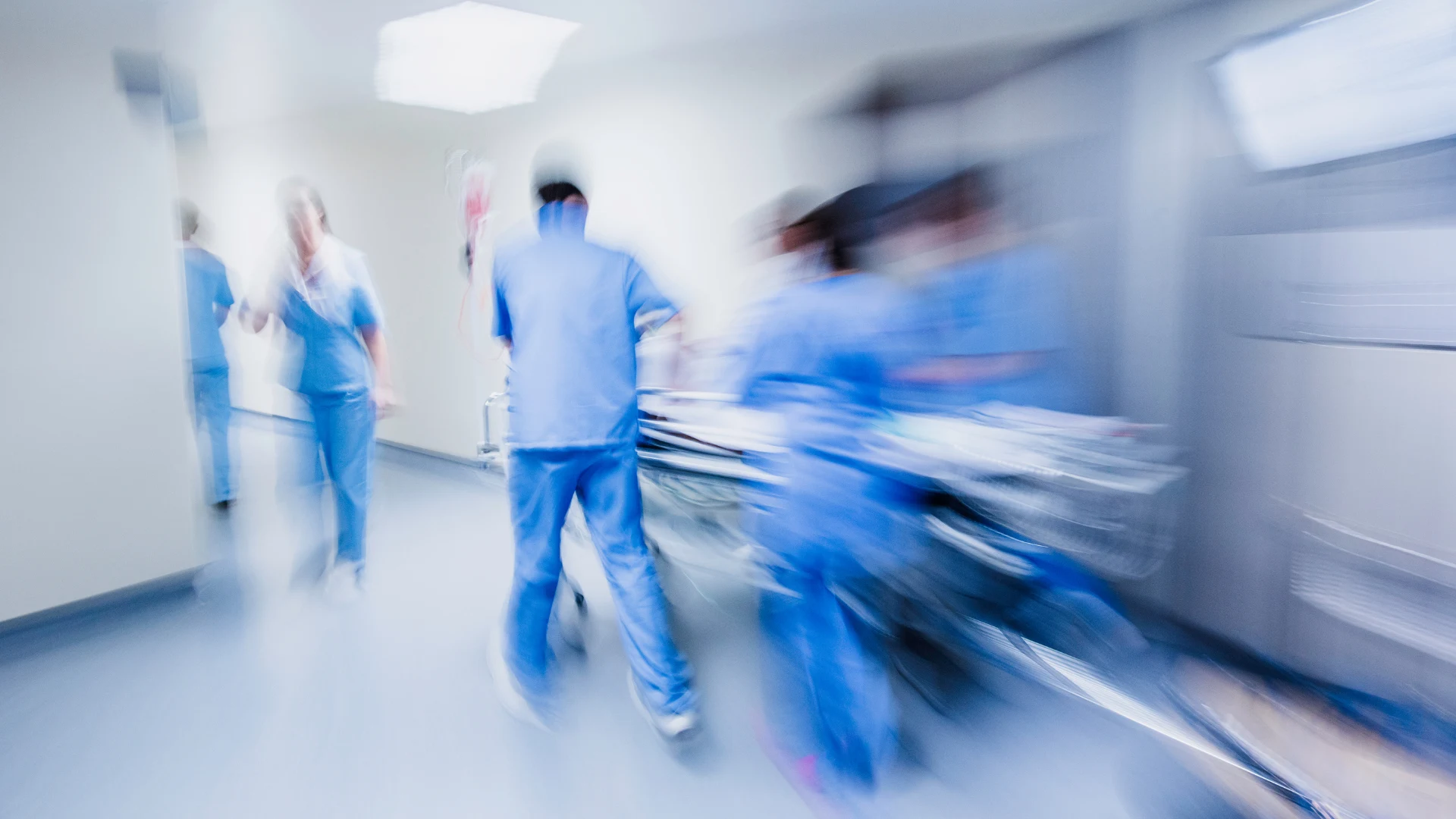 Blurred image of medical staff in blue scrubs pushing a hospital stretcher through a corridor.
