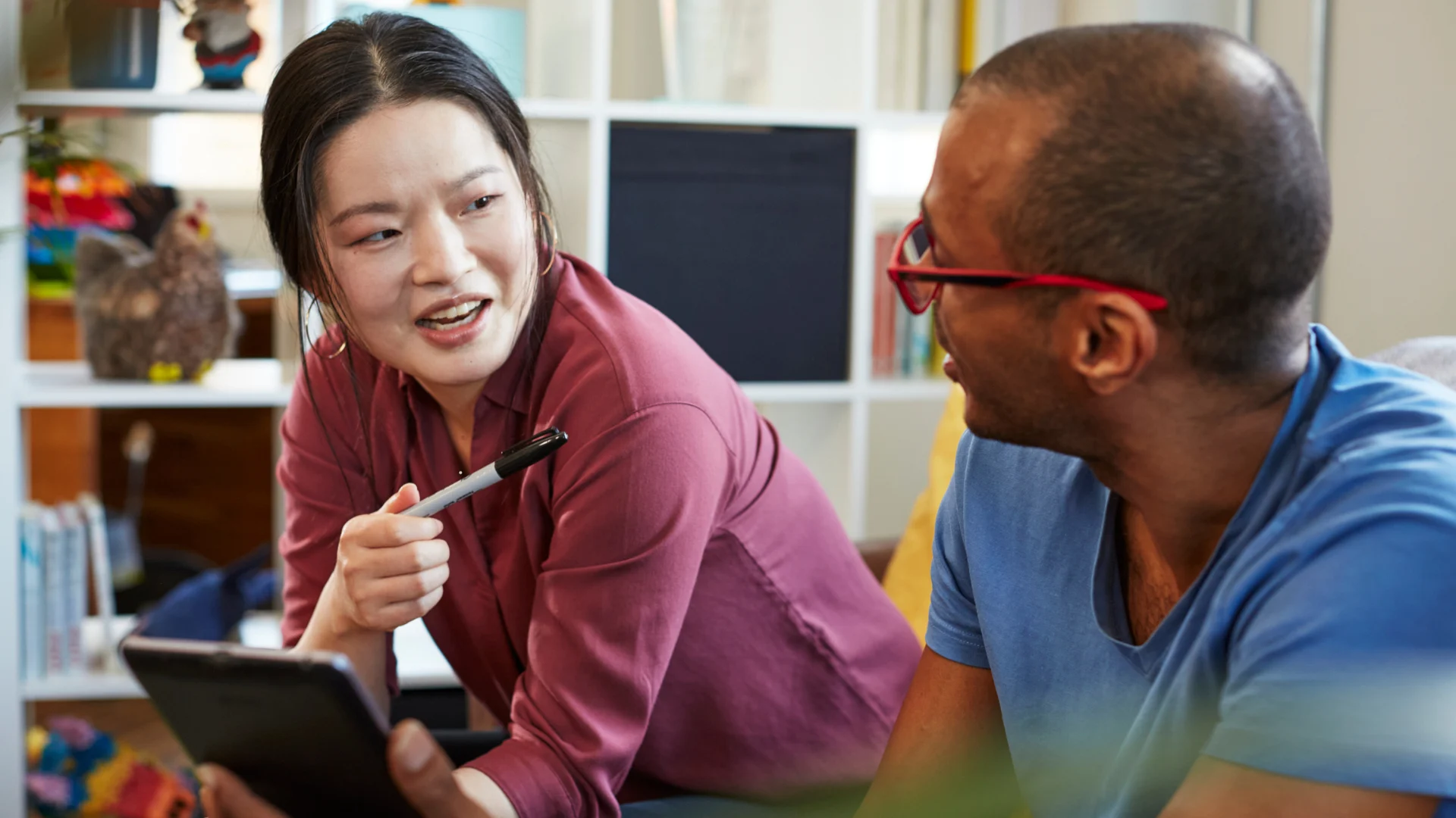 Two people sitting and having an engaged conversation, one holding a pen and the other holding a tablet.