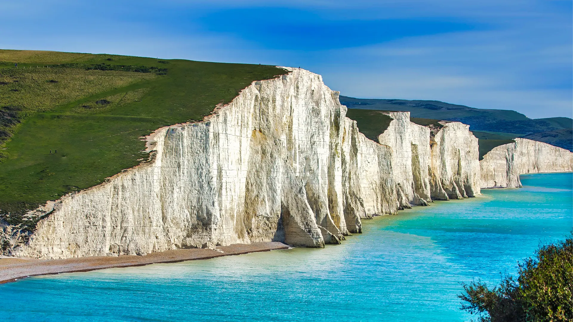 White chalk cliffs with green grassy tops overlooking a turquoise sea under a clear blue sky.