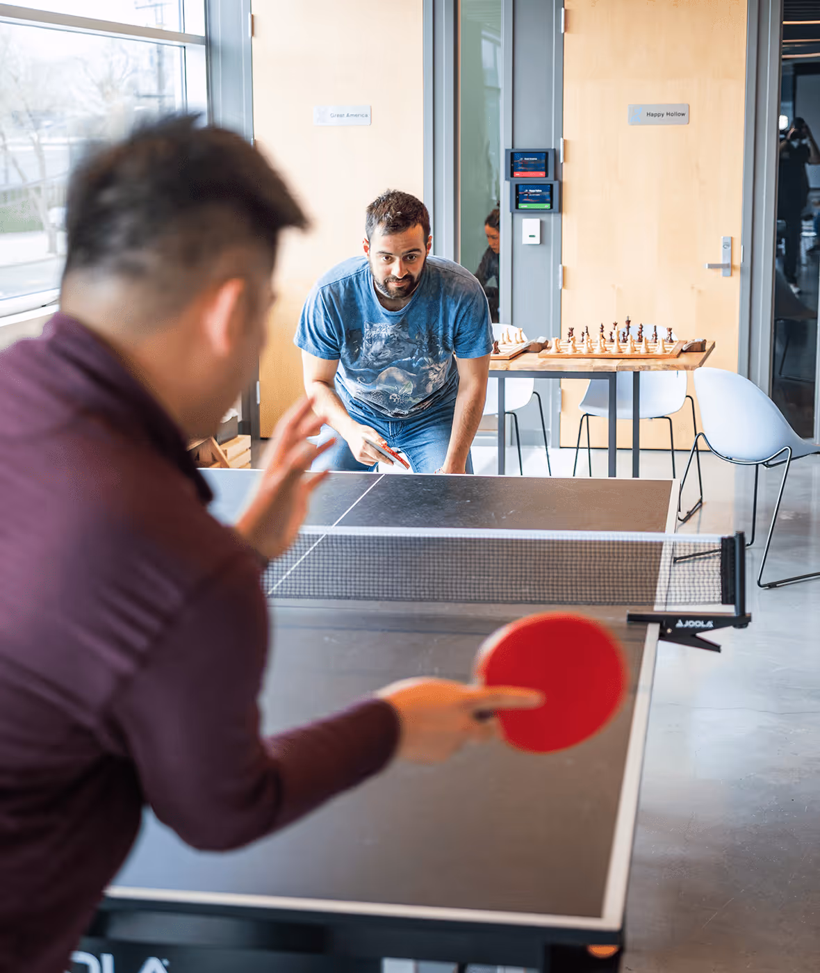 Two men are playing ping pong in the office