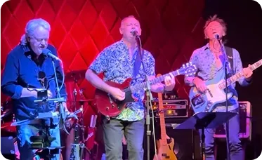 Victor Towle performing live on stage with two band members, all playing instruments and singing under vibrant red and purple stage lighting.