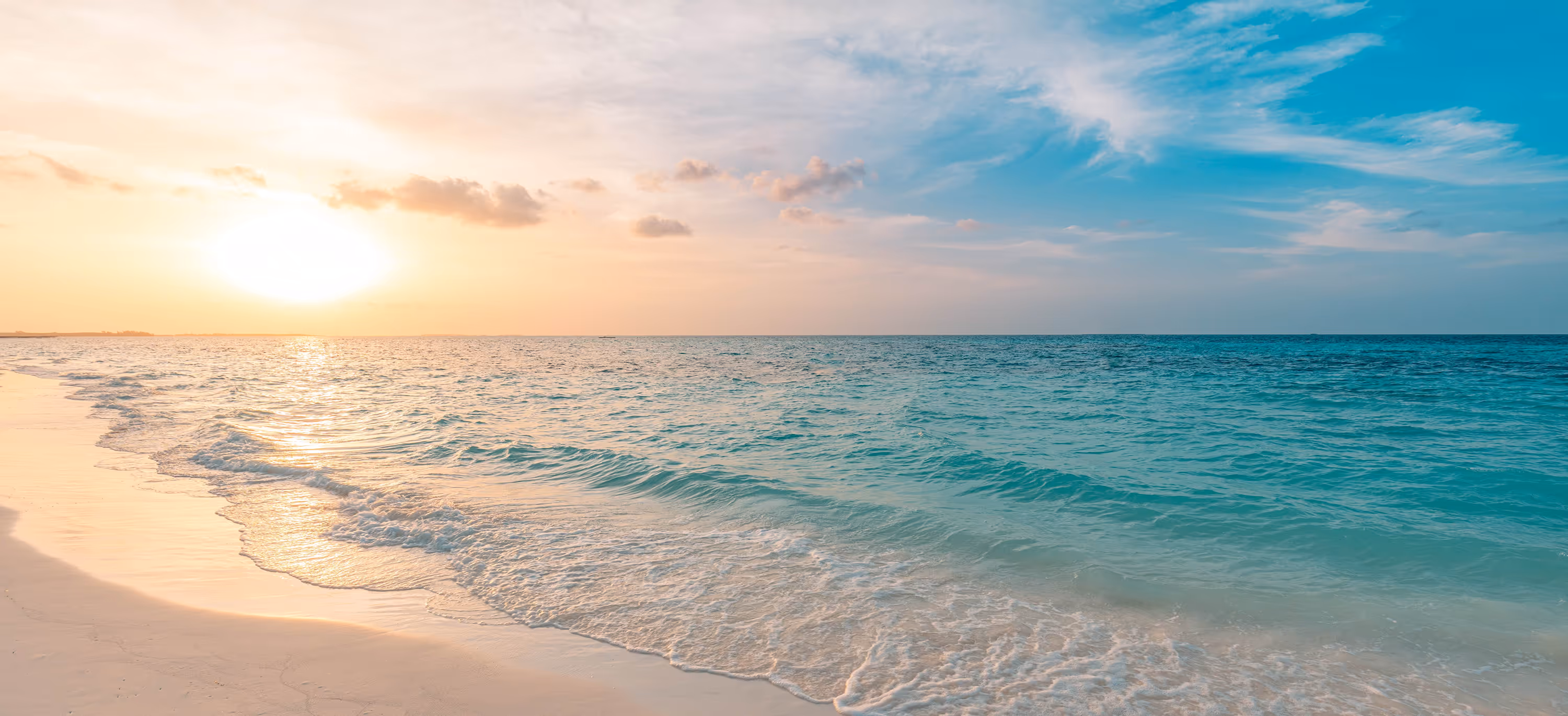 Golden sunset over a calm turquoise sea with gentle waves washing onto a soft sandy beach, perfect for a tranquil coastal escape.