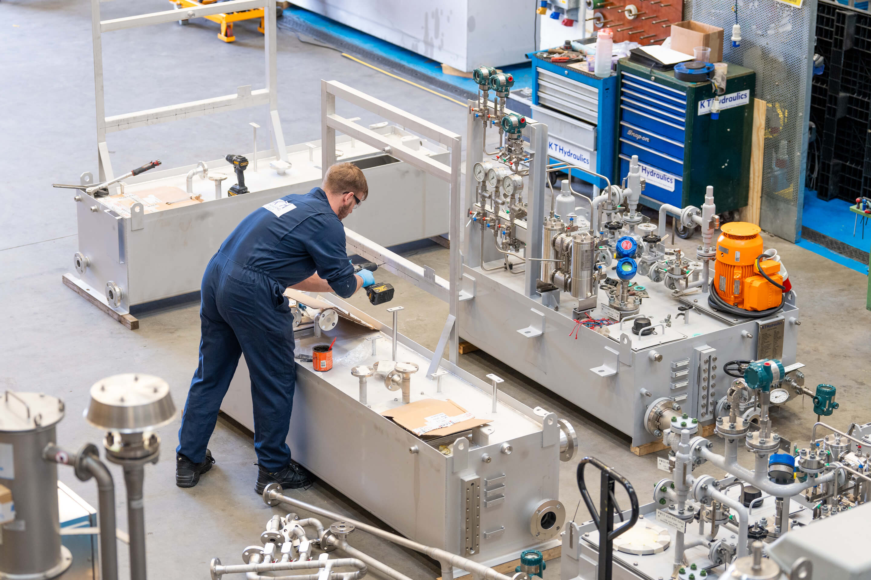 An employee drills into a piece of metal attached to some hydraulic equipment