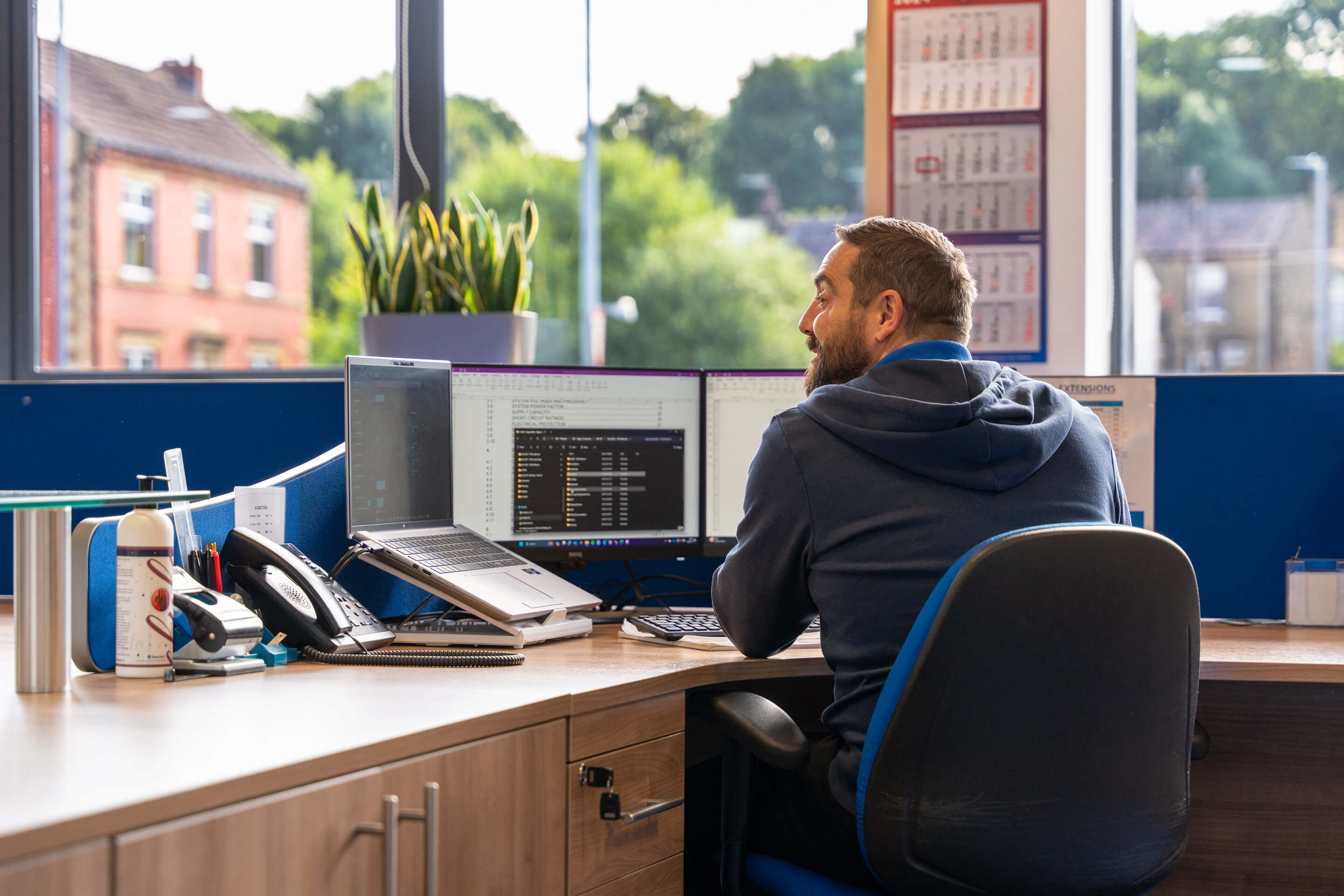 An employee sits at his desk, smiling in conversation with a colleague out of shot