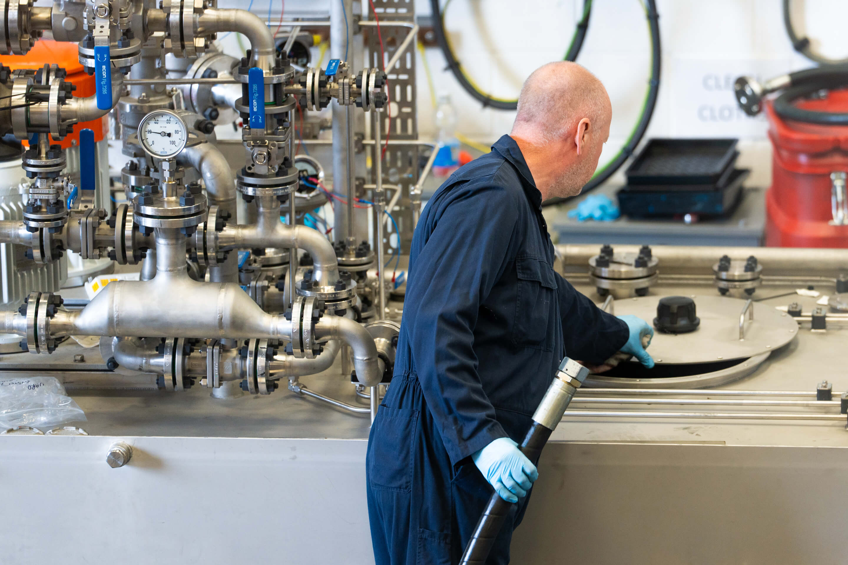 An employee hold a hose while opening the lid to a piece of hydraulic equipment 