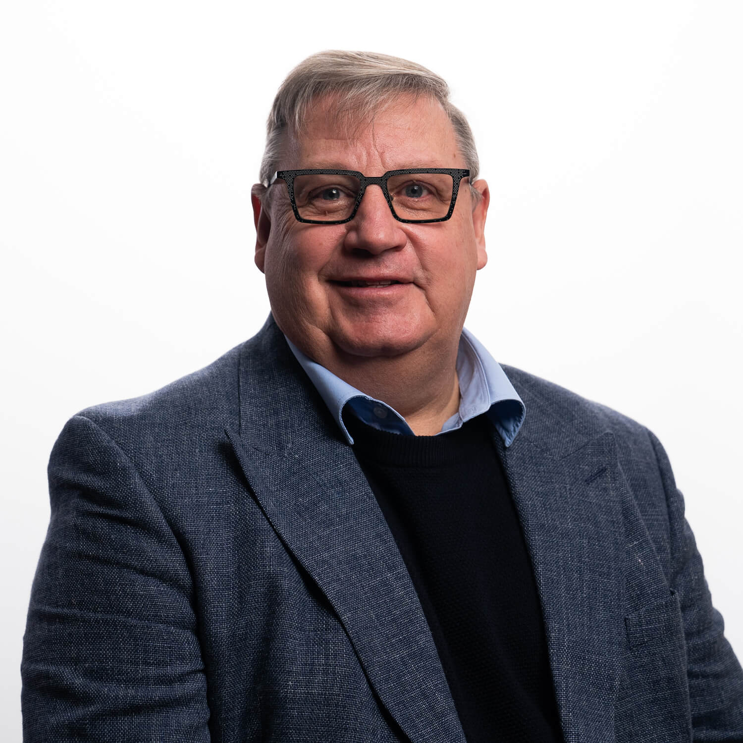 A portrait of Richard Ellis on a white background in blazer and jumper