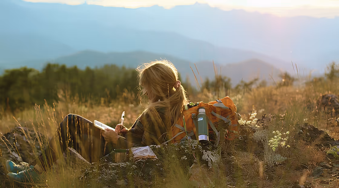Femme écrivant dans un carnet face aux montagnes, illustration de l’article blog sur l’écriture en trek.