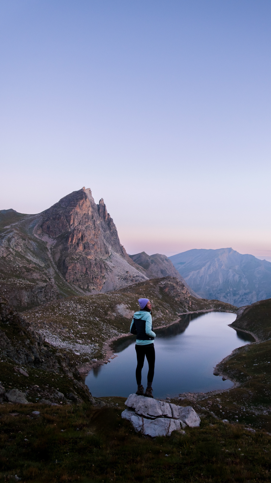 Femme observant un lac alpin entouré de montagnes dans les Écrins