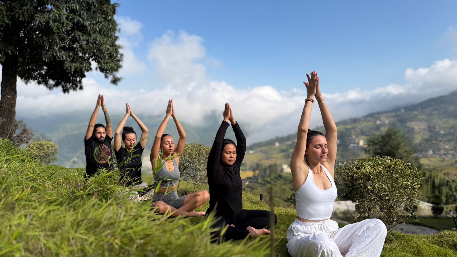 Groupe en séance de yoga en plein air face aux montagnes du Népal, mains jointes levées vers le ciel
