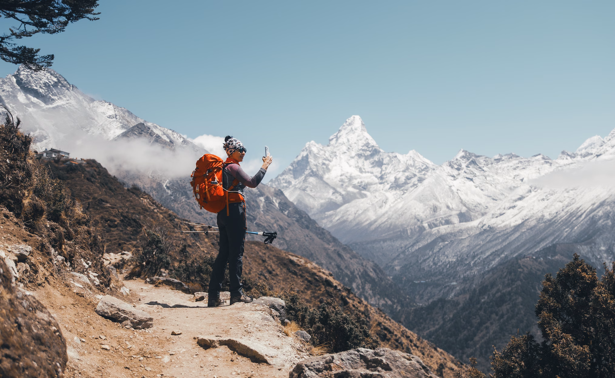 Trekkeur en veste bleue et sac à dos orange avançant sur une arête enneigée vers un sommet, au Népal.