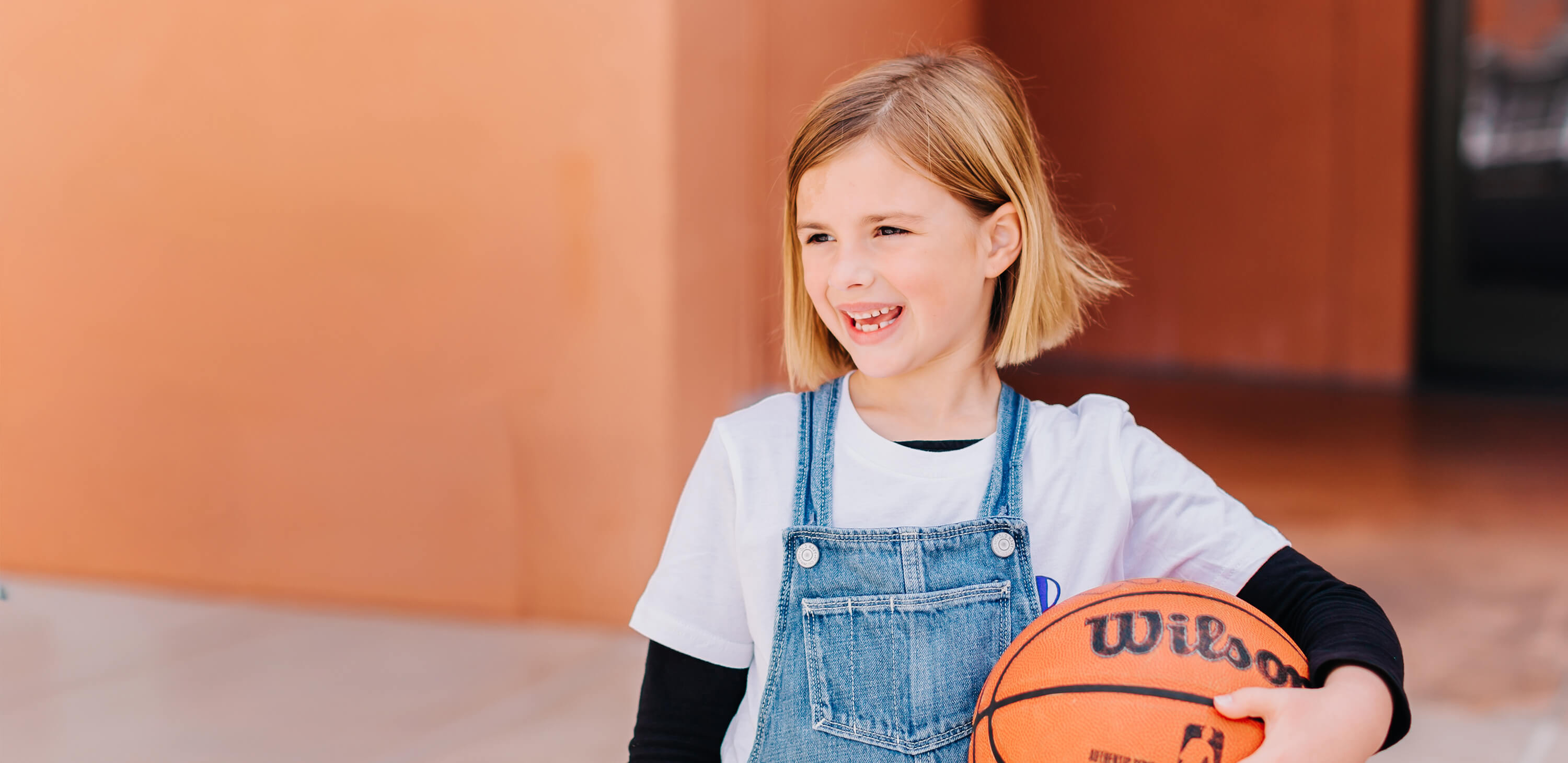 Smiling girl holding a basketball at a Bay Club camp