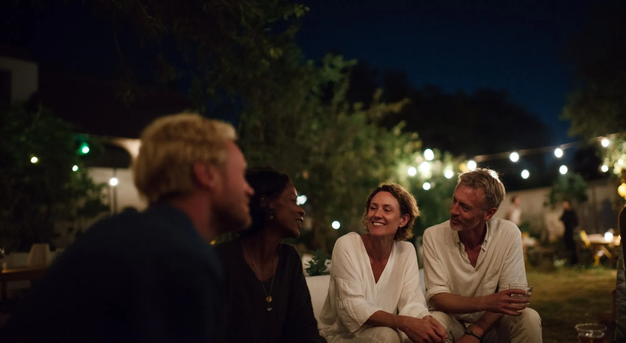 A group of friends sitting in a cozy backyard and enjoying a conversation in the evening.