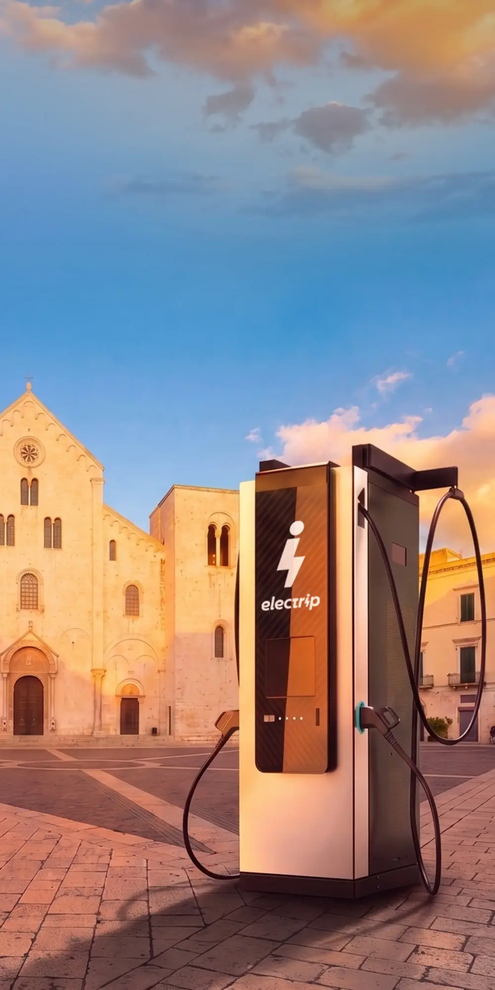 Colonnina di ricarica elettrica con logo electrip davanti a una chiesa storica al tramonto.