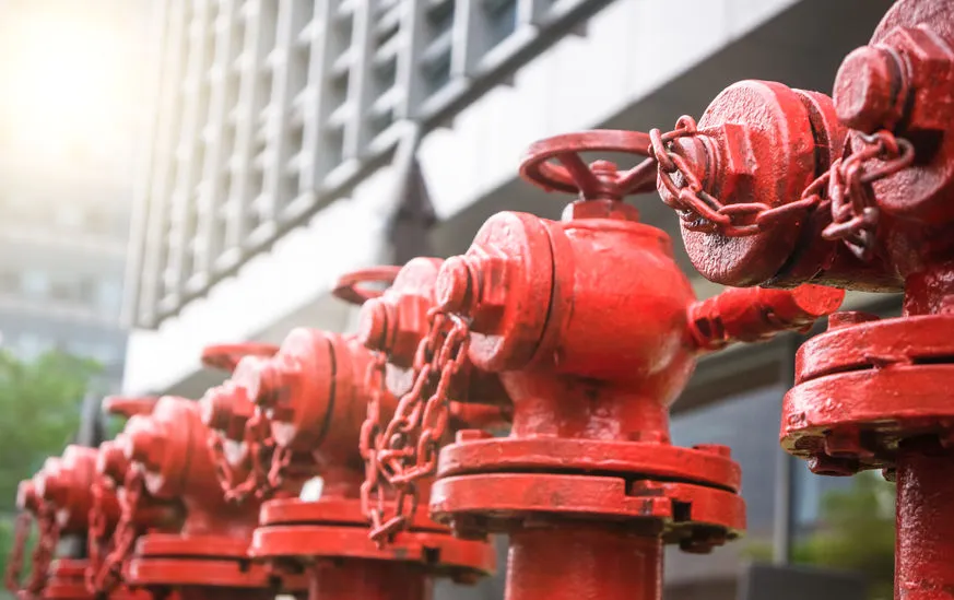 Red industrial piping system with vertical black pipes, pressure gauges, valves, and control devices in a utility room.